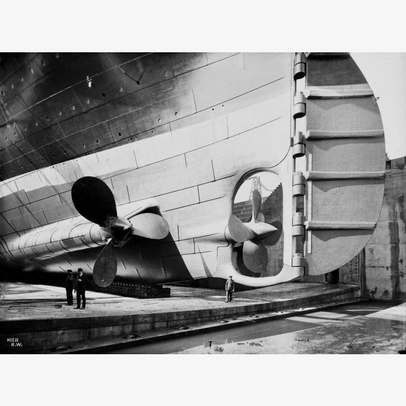 Triple propeller arrangement and rudder, portside view from dock floor, with three figures